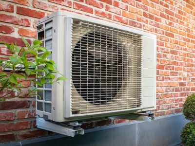 Air conditioning heat pump outdoor unit against brick wall.